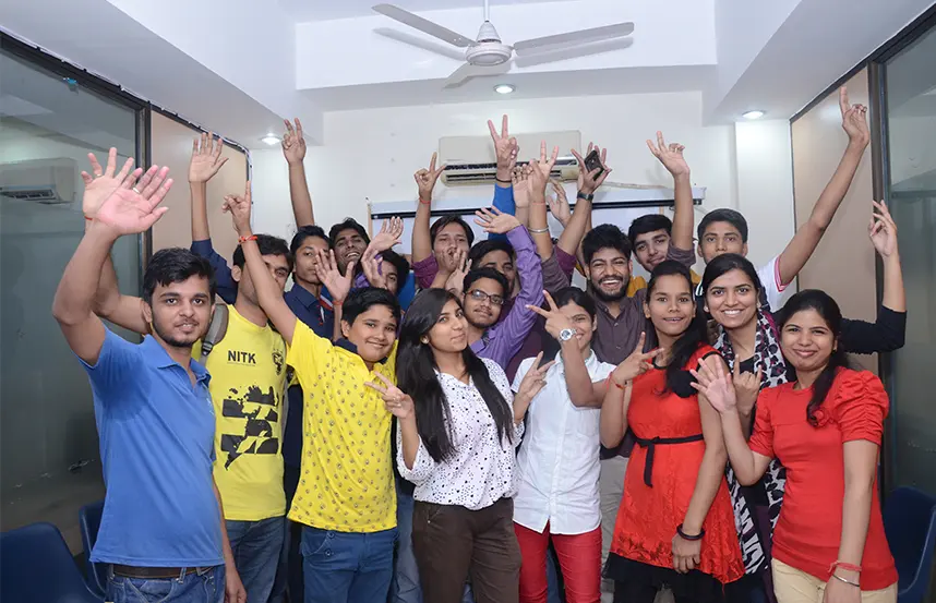 Cheerful group of students raising hands and posing in the classroom